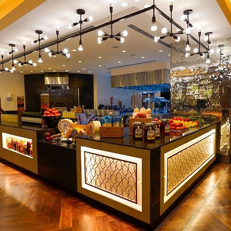 ホテル ジャバール オマール ハイアット リージェンシー マカー メッカ エクステリア 写真 The photo shows a stylish and modern buffet area in a restaurant or hotel. The design features a sleek counter with various food items displayed, including fresh fruits. The space is well-lit with pendant lights hanging from the ceiling, creating a w