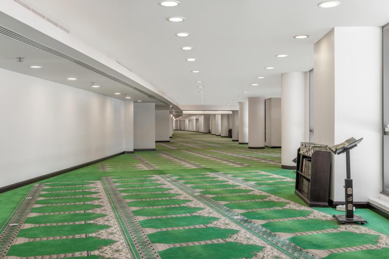 ホテル ジャバール オマール ハイアット リージェンシー マカー メッカ エクステリア 写真 The photo shows a spacious, well-lit indoor area with a green carpet designed for prayer. The carpet features a decorative pattern and outlines spaces where individuals would pray. There are white walls and several light fixtures in the ceiling provi