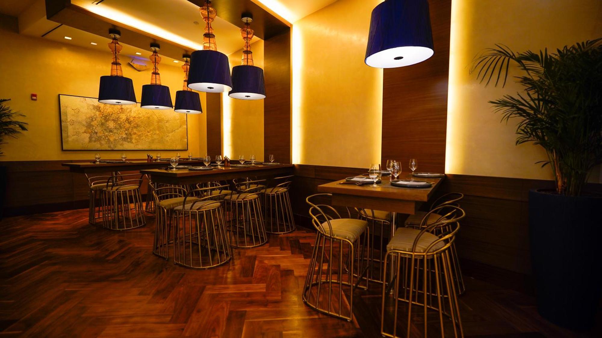 ホテル ジャバール オマール ハイアット リージェンシー マカー メッカ エクステリア 写真 The photo shows an elegantly designed restaurant interior. It features stylish seating arrangements with gold wire chairs paired with tables. The ambient lighting is warm, with a mix of recessed lights and pendant lamps that have blue shades, creatin
