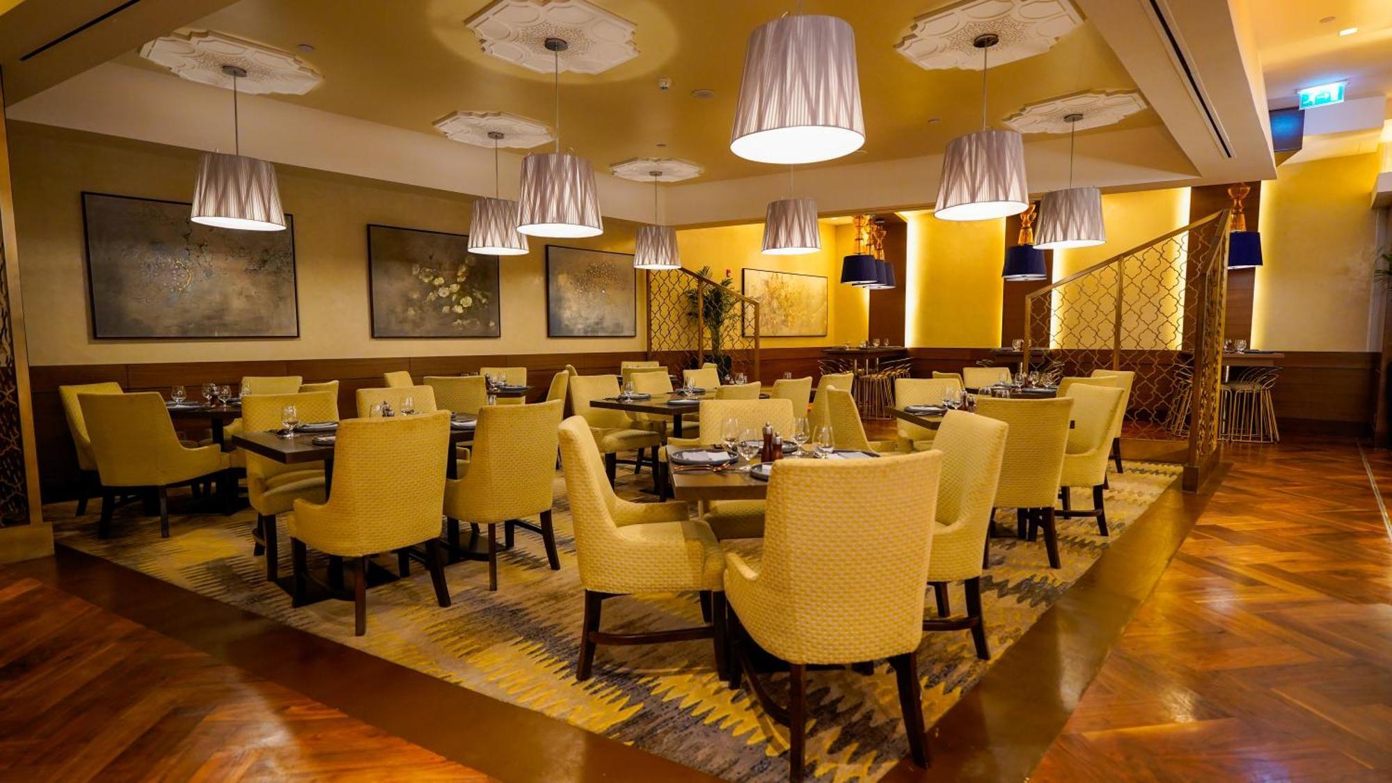 ホテル ジャバール オマール ハイアット リージェンシー マカー メッカ エクステリア 写真 The photo shows an elegant restaurant interior. There are several tables arranged with yellow upholstered chairs, creating a warm and inviting atmosphere. Soft lighting is provided by modern pendant lamps hanging from the ceiling. The floor features 