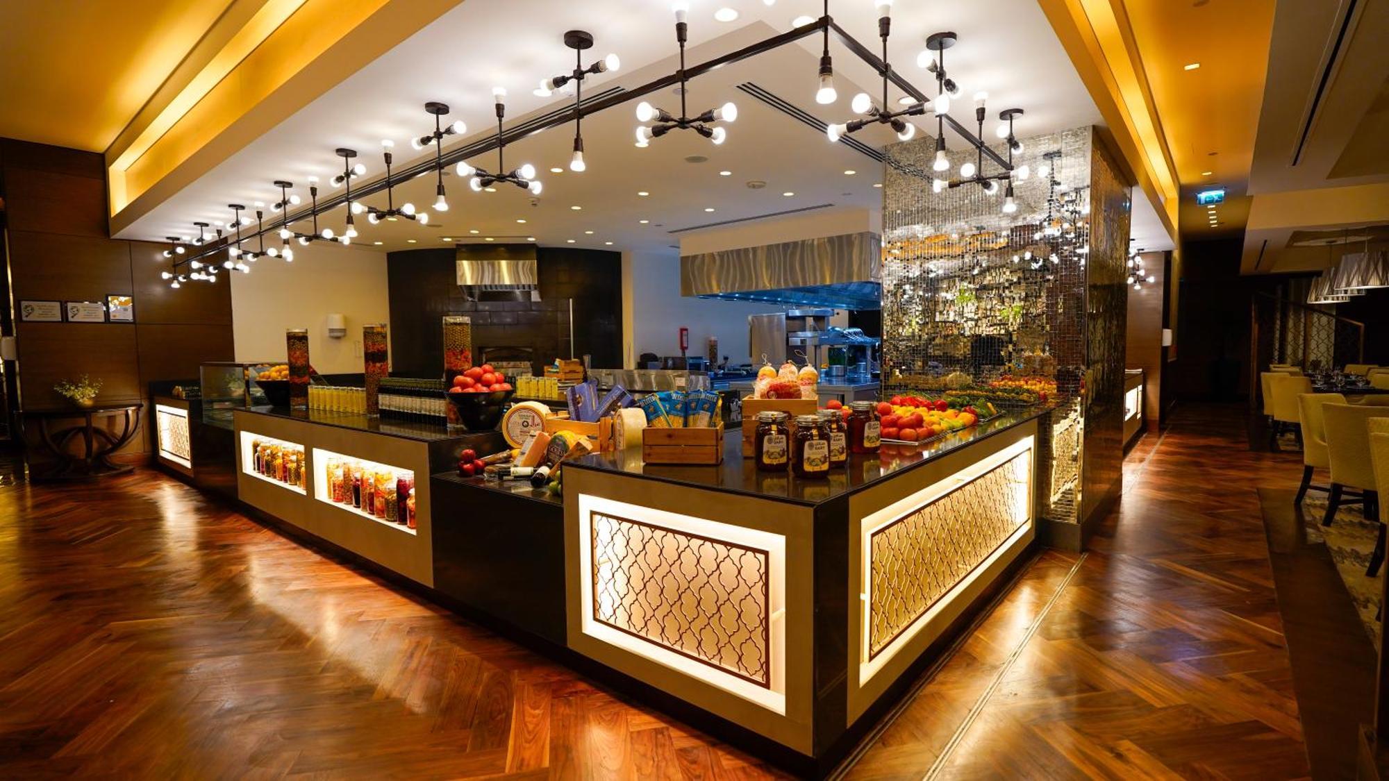 ホテル ジャバール オマール ハイアット リージェンシー マカー メッカ エクステリア 写真 The photo shows a stylish and modern buffet area in a restaurant or hotel. The design features a sleek counter with various food items displayed, including fresh fruits. The space is well-lit with pendant lights hanging from the ceiling, creating a w