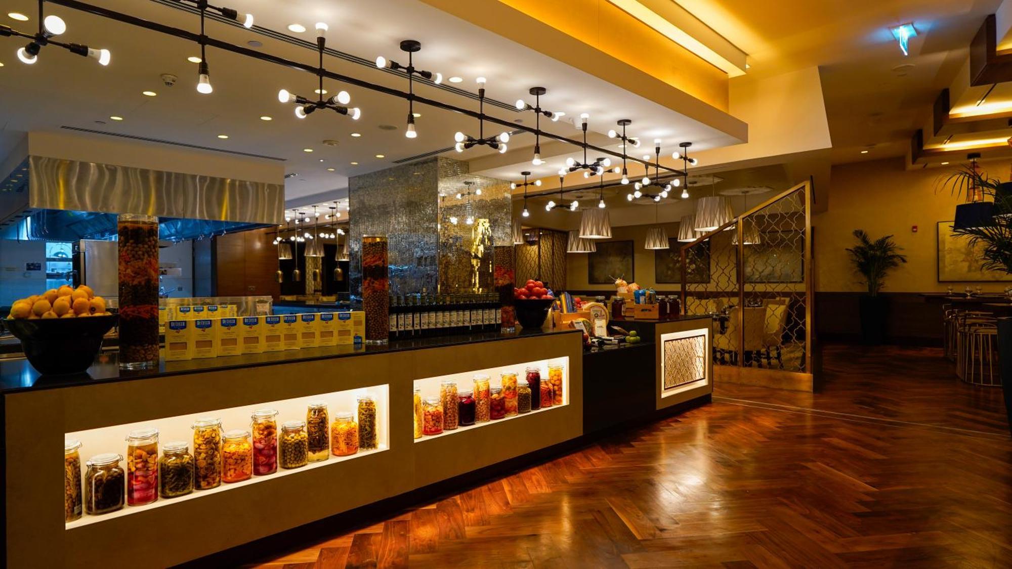 ホテル ジャバール オマール ハイアット リージェンシー マカー メッカ エクステリア 写真 The photo shows a stylish interior of a restaurant or café. It features a well-lit space with modern lighting fixtures hanging from the ceiling. The focal point is a counter area with jars filled with colorful ingredients or snacks, illuminated by li