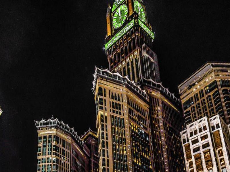 ホテル ジャバール オマール ハイアット リージェンシー マカー メッカ エクステリア 写真 The photo shows a tall building, which is a prominent feature of a city skyline, illuminated against a dark night sky. At the top of the building is a large clock tower, noticeable for its distinct green color, and intricate architectural details. Th
