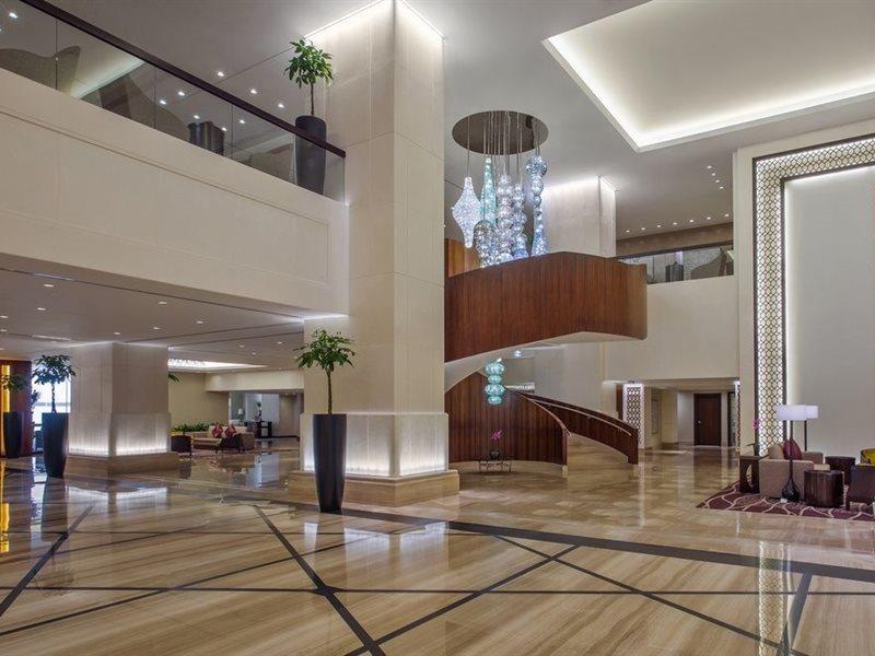 ホテル ジャバール オマール ハイアット リージェンシー マカー メッカ エクステリア 写真 The image shows a spacious and modern hotel lobby. It features elegant interior design with high ceilings and polished marble floors. A prominent wooden staircase with a stylish design is located in the center, leading to an upper level. There are de
