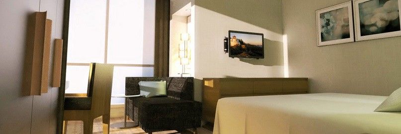 ホテル ジャバール オマール ハイアット リージェンシー マカー メッカ エクステリア 写真 The photo shows a modern hotel room or living space featuring a small seating area. On the left, there is a dark-colored couch and a glass side table. Across from the couch, mounted on the wall, is a flat-screen television. The room has light-colored