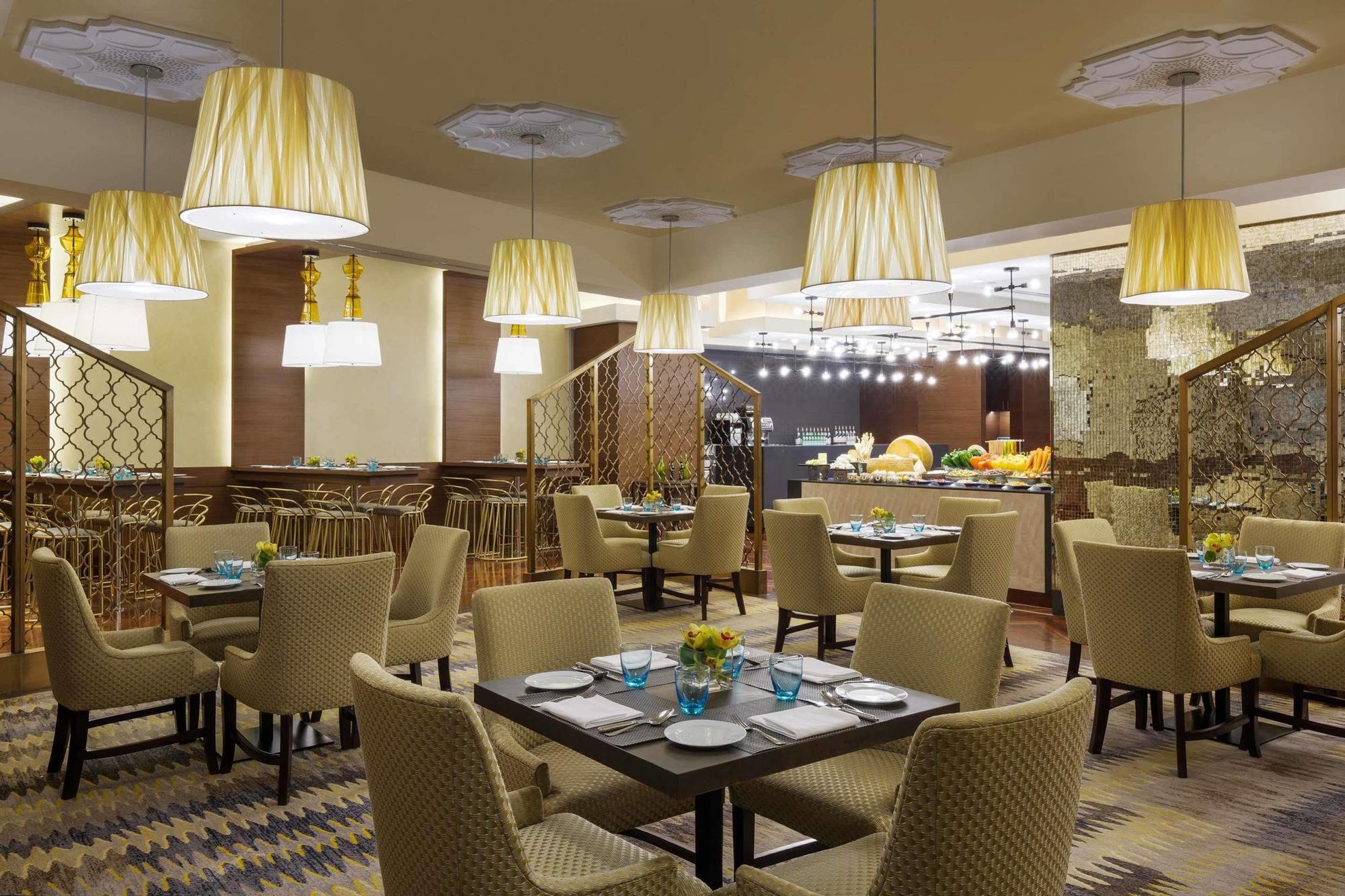 ホテル ジャバール オマール ハイアット リージェンシー マカー メッカ エクステリア 写真 The photo displays a modern restaurant interior. It features a series of round tables with beige upholstered chairs arranged neatly throughout the space. Each table is set with plates and blue-tinted glasses. The lighting is provided by stylish penda