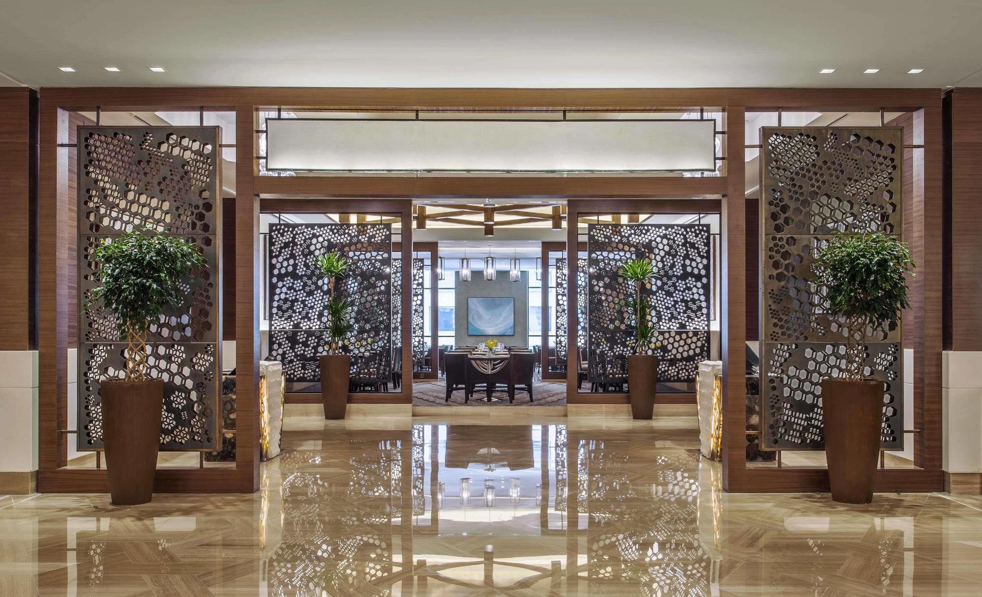 ホテル ジャバール オマール ハイアット リージェンシー マカー メッカ エクステリア 写真 The image shows an elegant interior space, likely the lobby or entrance of a luxurious hotel or restaurant. The area features decorative partitions with intricate designs, framed by wooden structures. These partitions create a sense of separation whi