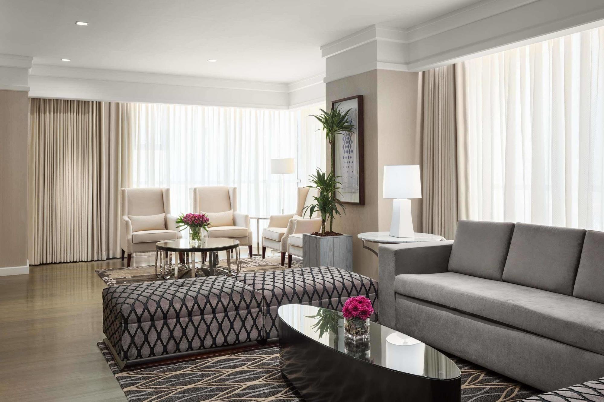 ホテル ジャバール オマール ハイアット リージェンシー マカー メッカ エクステリア 写真 The photo depicts a modern living room with a stylish and inviting design. There are large windows covered with light-colored curtains that allow natural light to fill the space. The furniture includes a gray sofa, a patterned ottoman with a geometri