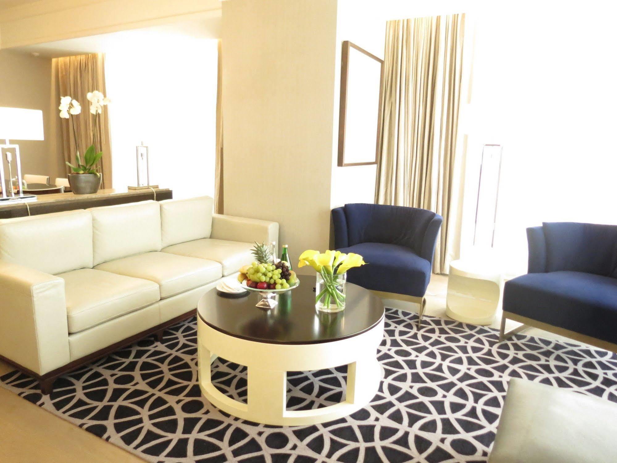 ホテル ジャバール オマール ハイアット リージェンシー マカー メッカ エクステリア 写真 The photo shows a stylish and modern living area. It features a white sectional sofa, two blue upholstered chairs, and a round black coffee table with a decorative centerpiece that includes flowers and fruits. The flooring is covered with a patterned