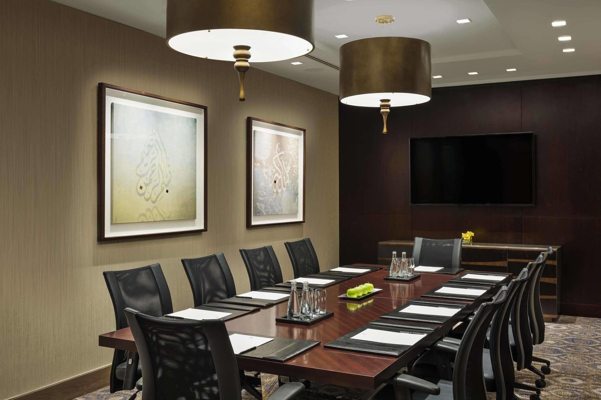 ホテル ジャバール オマール ハイアット リージェンシー マカー メッカ エクステリア 写真 The photo shows a modern conference room featuring a large wooden table that accommodates several black ergonomic chairs. Above the table, there are two stylish light fixtures hanging from the ceiling. The walls are decorated with two framed abstract