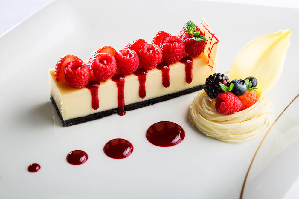 ホテル ジャバール オマール ハイアット リージェンシー マカー メッカ エクステリア 写真 The photo shows an elegantly plated dessert featuring a rectangular piece of cheesecake topped with fresh raspberries. The cheesecake is set on a dark crust, possibly made of chocolate or cookie crumbs. There are red fruit coulis drizzled artfully ar