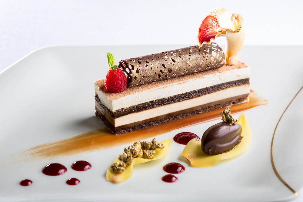 ホテル ジャバール オマール ハイアット リージェンシー マカー メッカ エクステリア 写真 The photo showcases an elegantly plated dessert. It features a layered cake with different textures and flavors, including chocolate and cream layers. The dessert is topped with a decorative chocolate tube and garnished with fresh raspberries and a s