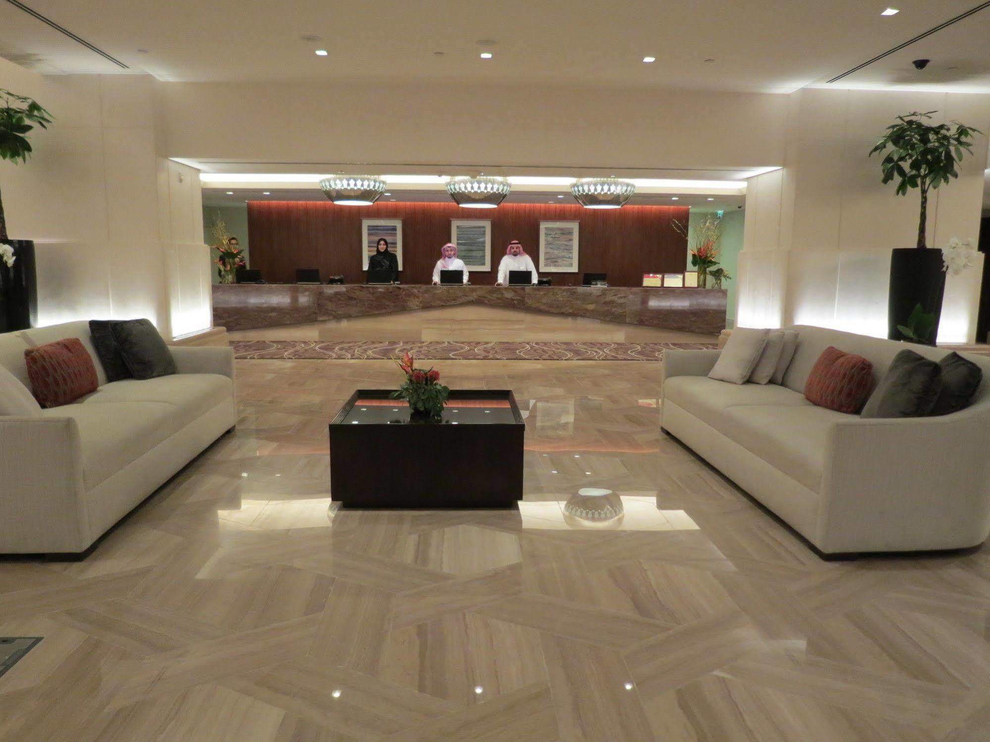 ホテル ジャバール オマール ハイアット リージェンシー マカー メッカ エクステリア 写真 The photo shows a modern hotel lobby. In the foreground, there are two light-colored sofas with decorative pillows, positioned facing each other. A small coffee table with a plant sits between the sofas. 

In the background, there is a reception desk