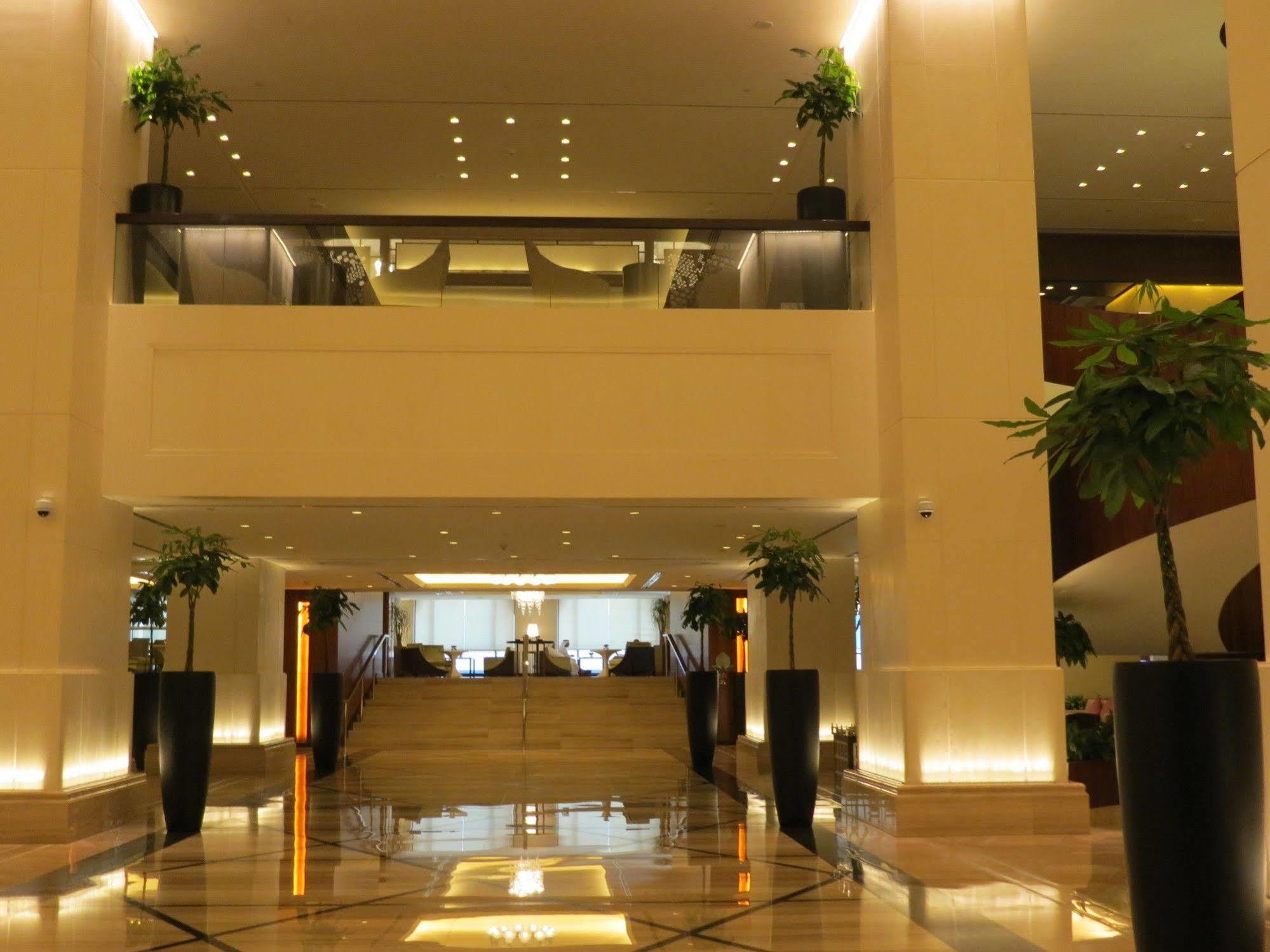 ホテル ジャバール オマール ハイアット リージェンシー マカー メッカ エクステリア 写真 The photo shows a spacious and elegantly designed hotel lobby. It features a multi-level layout with a set of stairs in the center leading to an upper floor. The lobby is well-lit with a warm glow from recessed lighting, and there are decorative plan