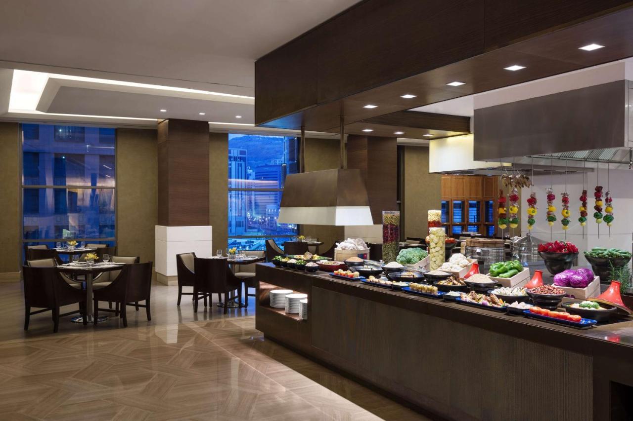 ホテル ジャバール オマール ハイアット リージェンシー マカー メッカ エクステリア 写真 The photo shows a dining area, likely within a restaurant or buffet setting. On the right side, there is a long food display featuring various dishes, likely consisting of fruits, vegetables, and other culinary items. The area is well-lit, with moder