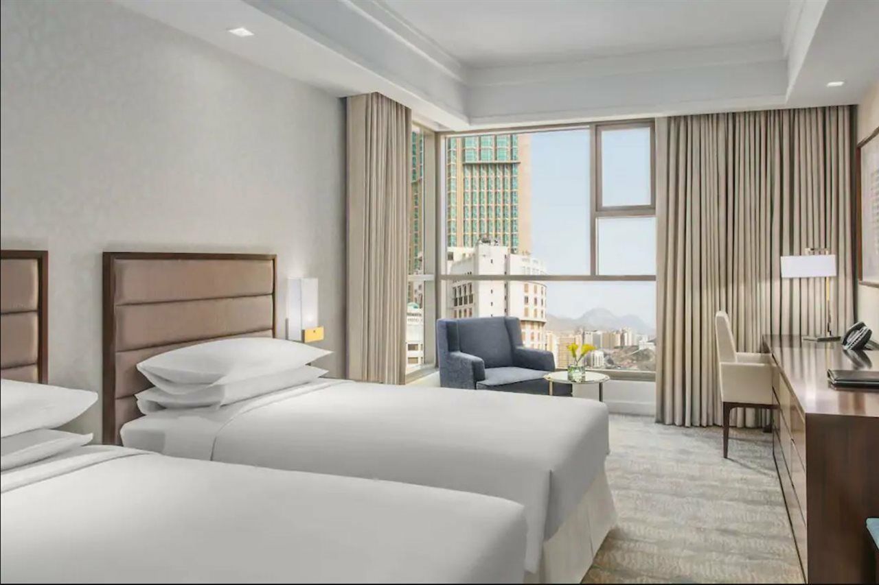ホテル ジャバール オマール ハイアット リージェンシー マカー メッカ エクステリア 写真 The photo shows a modern hotel room featuring two beds with white linens. The room has a bright and airy feel, thanks to large windows that allow natural light to flood in. There are floor-to-ceiling curtains, and a small seating area with a chair an