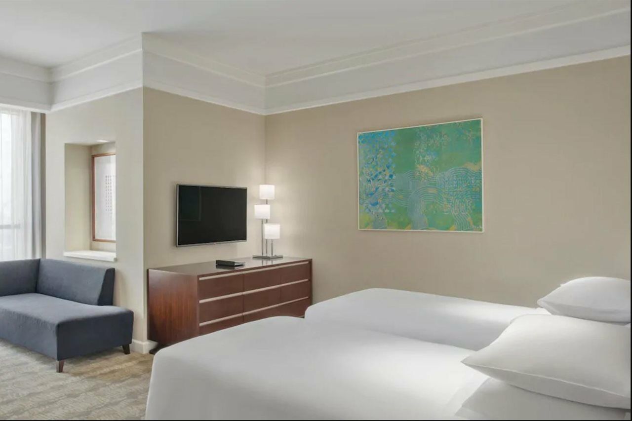 ホテル ジャバール オマール ハイアット リージェンシー マカー メッカ エクステリア 写真 The photo shows a hotel room featuring two twin beds with white bedding. A dark wooden dresser is positioned against one wall, with a flat-screen TV mounted above it. Next to the dresser, there are two modern lamps providing soft lighting. On the wal